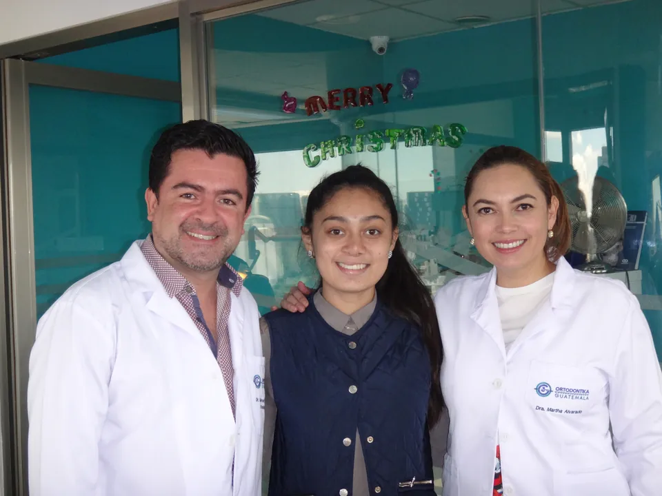 Dos especialistas de la Fundación Sonrisa 502 con bata blanca junto a una paciente adolescente