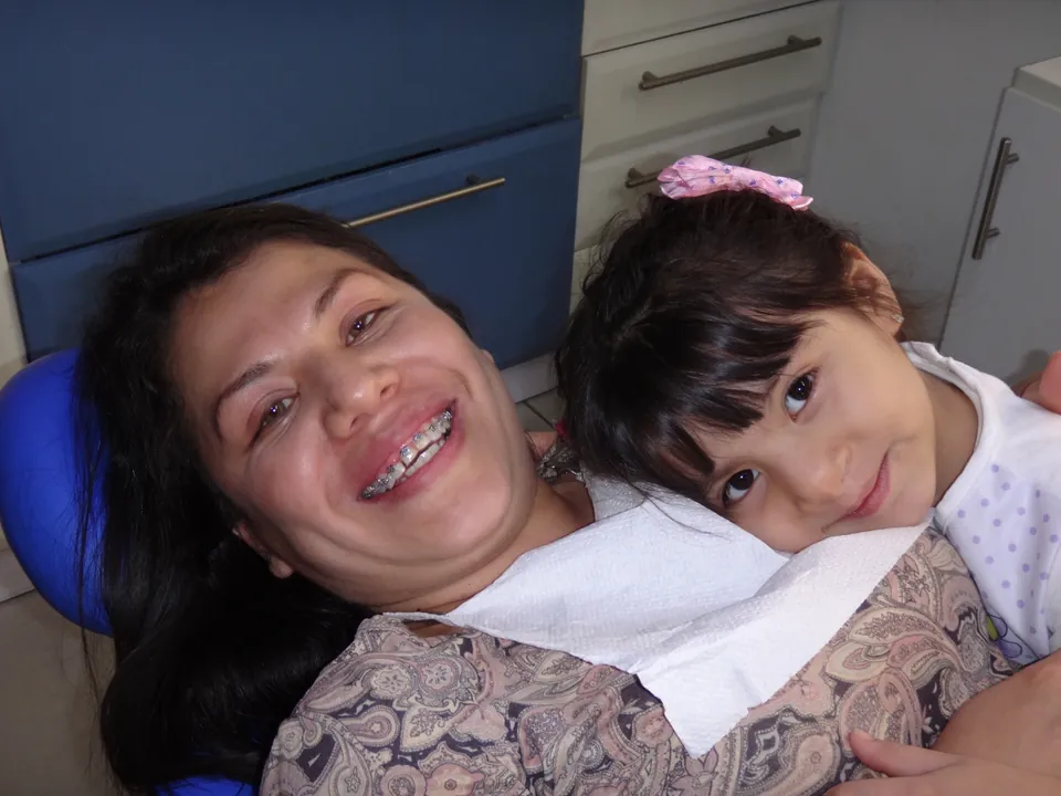 Madre e hija sonriendo juntas en el sillón de la clínica dental